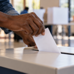 Illustration of a voter placing a ballot into a ballot box at a polling place.